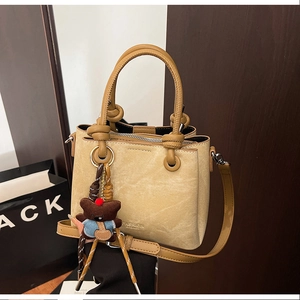 Close-up of yellow faux leather bucket bag with fashion logo and brown bear pendant