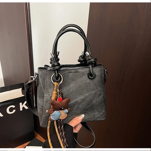 Detail of grey denim bucket bag with black leather handle and brown plush bear charm
