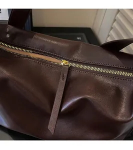 Close-up of a smooth gold metal zipper and matching leather puller on a brown tote bag