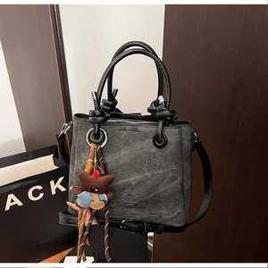 Detail of vintage gray denim bucket bag with teddy bear charm and leather strap