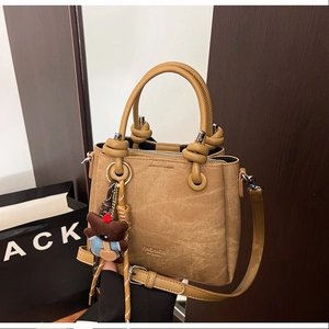 Macro detail of brown woven texture handbag with teddy bear charm and sleek handles