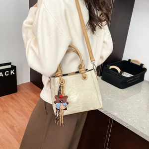 Close-up of beige bucket bag with brown handles and a cute bear charm on a model