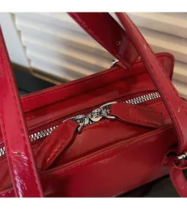 Detail of red patent leather shoulder bag showing smooth silver double zipper hardware