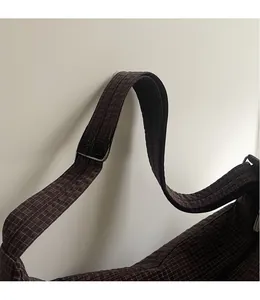 Detail view of the brown checkered bag showing its smooth adjustable long shoulder strap