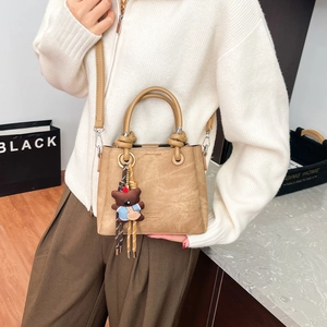 Detail of khaki bucket bag featuring round handles and a cute plush bear charm