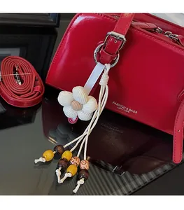 Detail of red leather tote bag featuring a white woven flower charm and beaded tassel