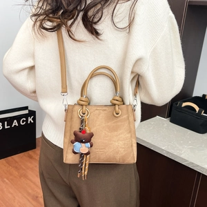 Brown bucket bag with cute bear charm and tassel shown on model in home setting