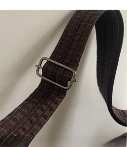 Detail of adjustable silver buckle on dark brown checkered canvas strap crossbody bag