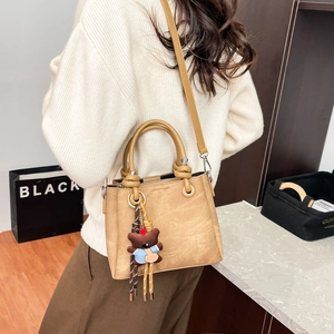 Model view of a light brown bucket bag with dual handles and a bear charm accessory