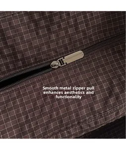 Detail of silver polished metal zipper slider on a dark brown checkered fabric bag