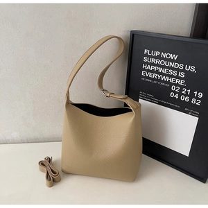 Detail of beige pebble leather bucket bag featuring wide handle and extra shoulder strap