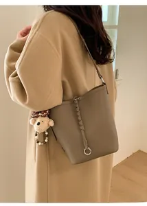 Dettaglio borsa a secchiello in pelle marrone con decoro intrecciato e ciondolo orso