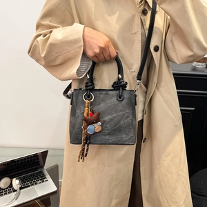 Detail of dark gray canvas bucket bag with bear pendant and leather handles in office setting