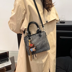 Detailed texture of grey denim bucket bag with leather handles and a cute bear charm
