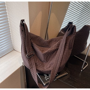 Detail of adjustable strap and brown checkered fabric on a crossbody dumpling bag