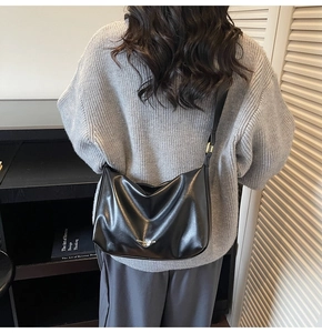 Close-up of black leather shoulder bag with logo detail on a model in a minimal setting