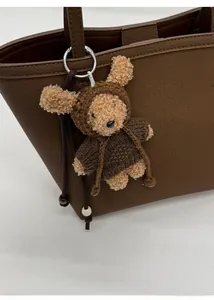 Detailed view of a brown plush bear keychain in a knitted hoodie on a leather tote bag
