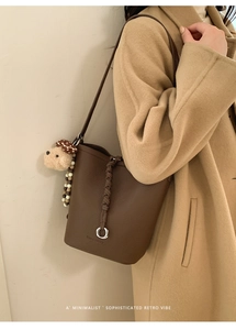 Dettaglio borsa a secchiello in pelle martellina marrone con tracolla intrecciata e orsetto