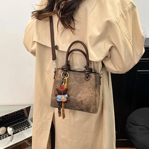 Detailed view of a retro brown bucket bag with a plush bear charm on an office desk