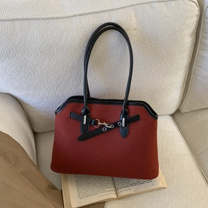 Detail of red-brown textured tote bag with black straps and silver buckle on a sofa