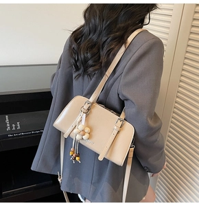 Detail of a beige leather shoulder bag featuring decorative buckles and floral bead charm