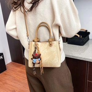 Detail of vintage beige bucket bag with round handles and a cute bear plush pendant