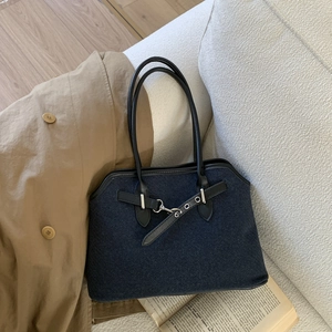 Detail of dark blue denim handbag with black leather handles and silver metal hardware accents