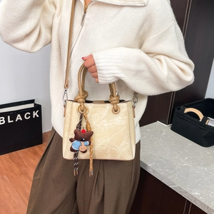 Detail of cream bucket bag featuring vintage rock texture and cute bear charm pendant