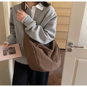 Detailed view of a brown plaid crossbody tote bag worn by a model in a cozy indoor setting