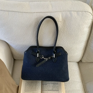 Detail of dark blue denim tote bag with black leather straps on a beige sofa