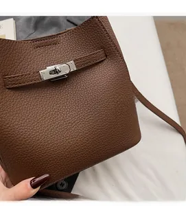 Close-up of brown litchi grain leather texture and silver buckle hardware on a bucket bag