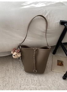 Dettaglio borsa a secchiello color cammello con finiture intrecciate e ciondolo orso