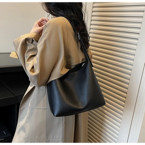 Detail of black lychee grain leather bucket bag worn with a khaki trench coat