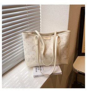 Detail of cream tote bag with rabbit patterns and metal logo on a windowsill