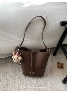 Dettaglio della borsa a secchiello in pelle marrone con ciondolo a forma di orsetto