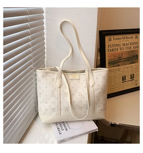 Close-up of cream PU leather tote bag with rabbit print and gold metal nameplate