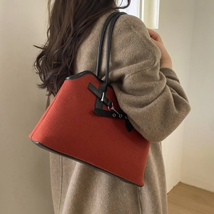 Close-up of brick red felt shoulder bag with black leather straps and buckle detail