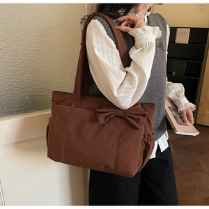 Close-up of brown nylon tote bag with large decorative bow and side elastic pocket