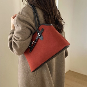 Detail of red canvas tote bag with black leather straps and decorative belt buckle
