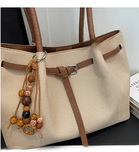 Detail of canvas tote bag featuring leather straps and decorative wooden bead tassel