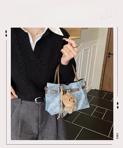Detail of blue denim tote bag with brown leather handles and cute bear charm