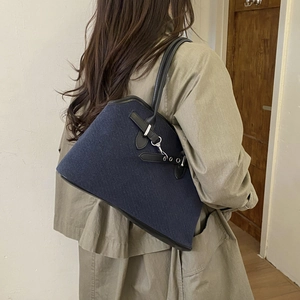 Detail view of navy denim tote bag with leather straps and silver buckle on model back