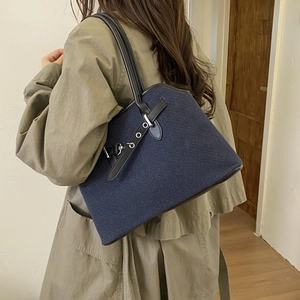 Detail of dark blue denim tote with black leather straps and retro buckle on model