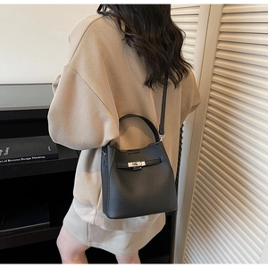 Side view of black lychee leather bucket bag with metallic twist lock on female model