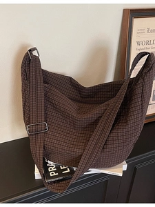 Brown plaid large capacity crossbody bag with adjustable wide strap on a modern black cabinet