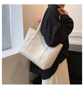 Detail of white tote bag with bear print and LUOMEN 1983 label on a model's shoulder