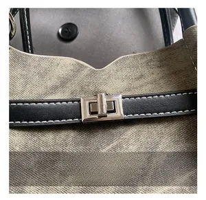 Macro shot of silver metal turn-lock closure on gray canvas bag with black leather straps
