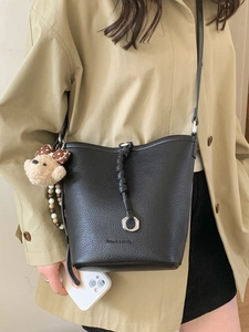 Borsa a secchiello minimalista in pelle nera con ciondolo a orso indossata con trench
