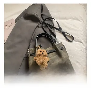 Detail of dark olive canvas tote bag with black leather straps and plush bear charm