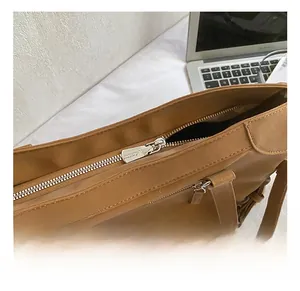 Detail view of large brown tote bag with smooth texture, silver zipper, and leopard charm